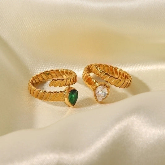 Two gold adjustable rings with a ridged band on fabric. One ring has a green teardrop stone, the other has a clear, diamond-like teardrop stone.
